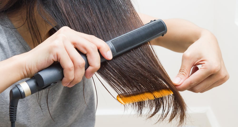 A woman is straightening her hair using a flat iron