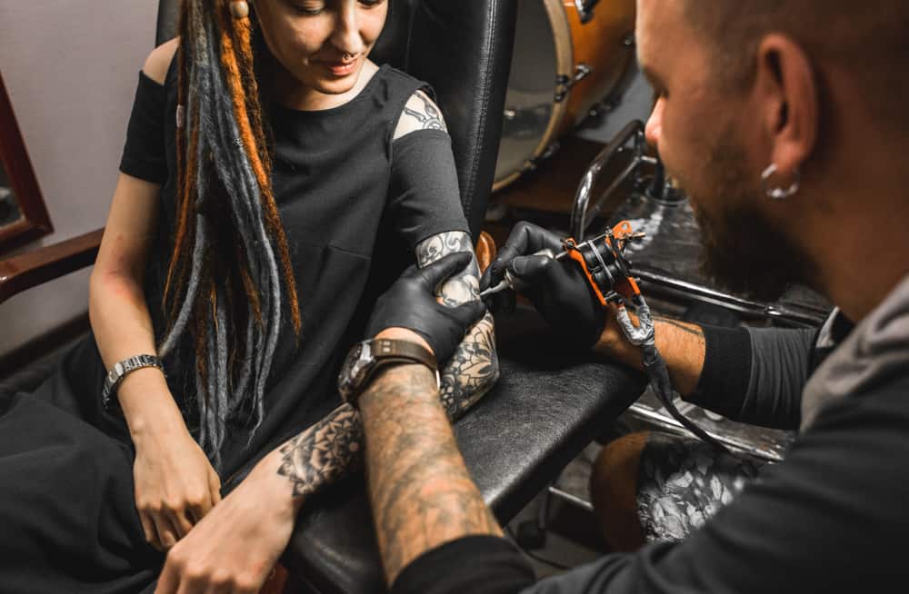 dreadlocked girl being tattooed