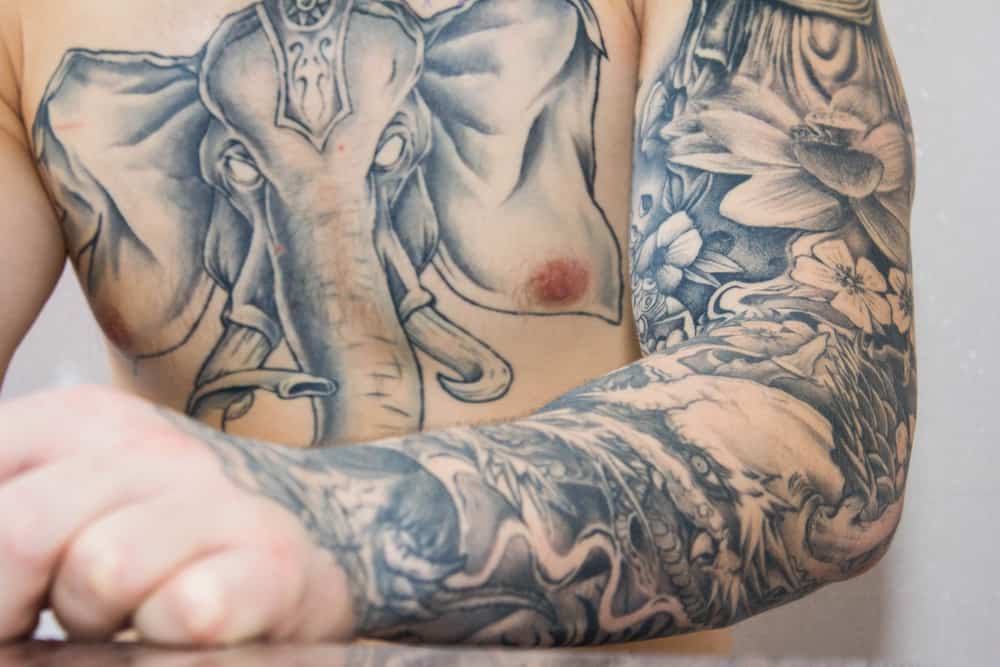 man’s tattooed arm and chest with an elephant tattoo