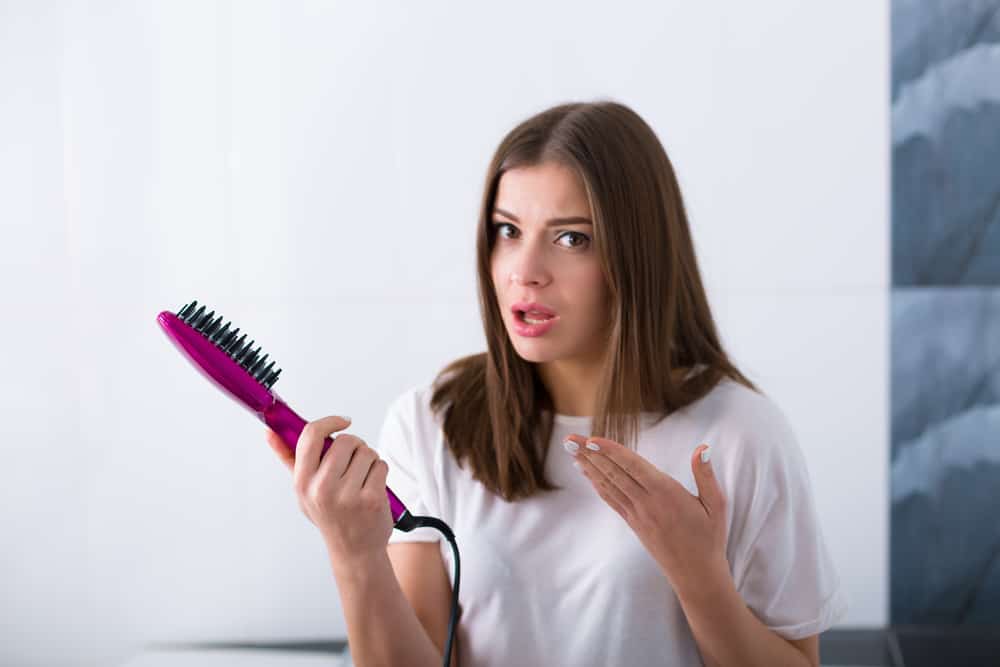 A woman is speaking; she holds a hot air hairbrush in her hand