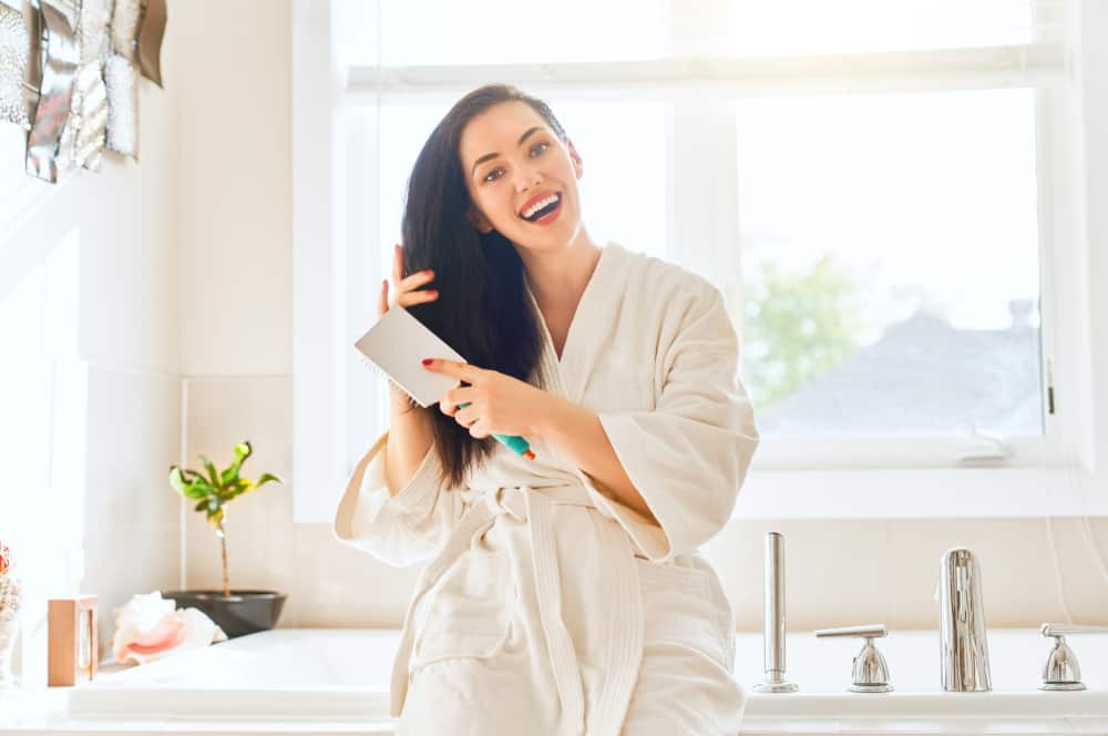 A woman smiles as she combs her hair in the bathroom