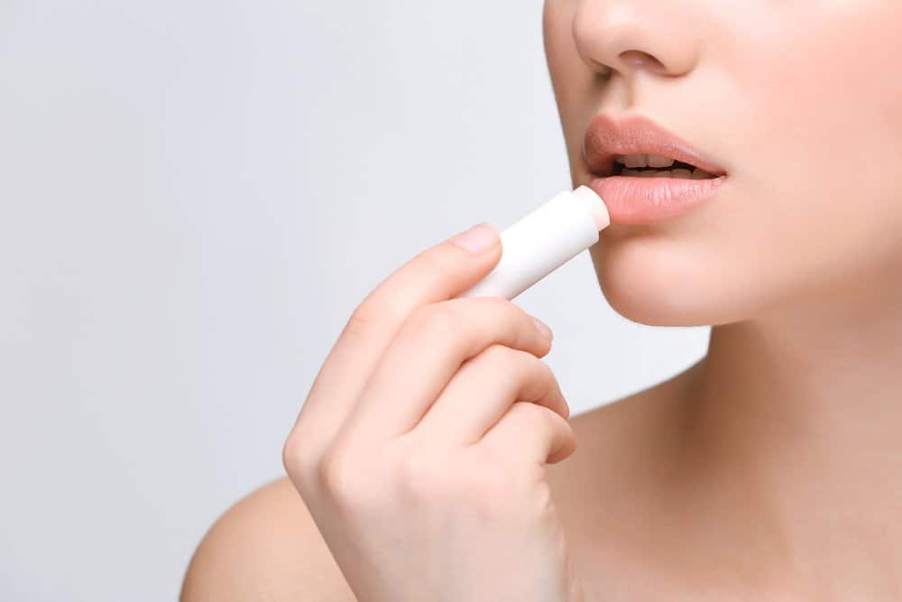 woman applying clear lip balm onto nude lips