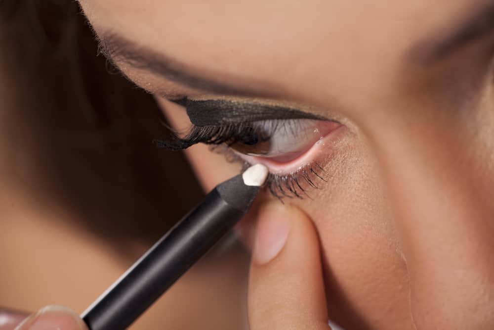 woman applying white eyeliner to the waterline