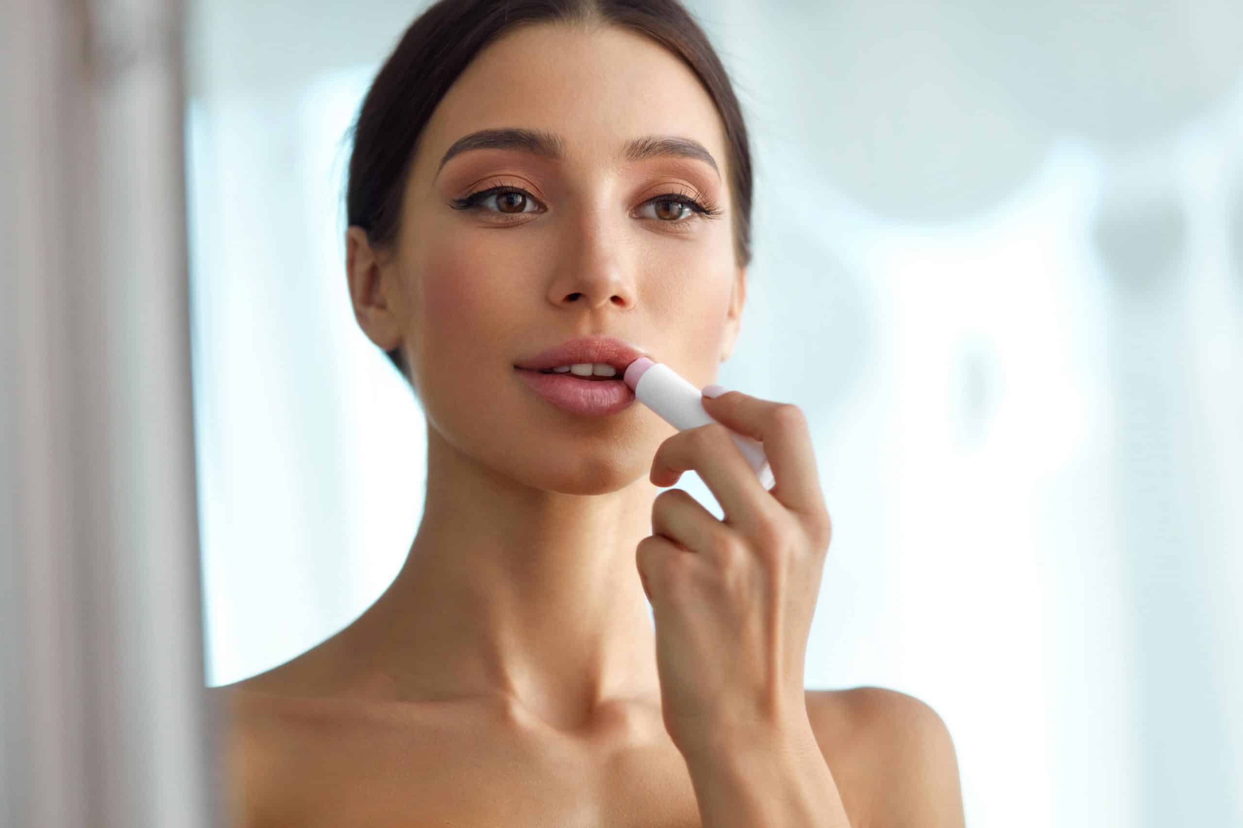 woman looking in mirror and applying lip balm on herself