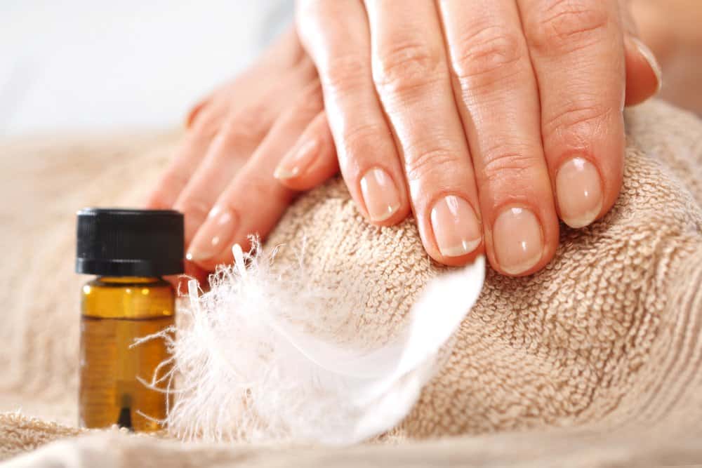 Manicured hands draped on a towel with a bottle of cuticle oil nearby