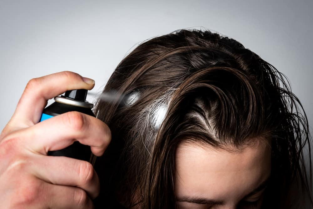 woman applying dry shampoo to oily hair