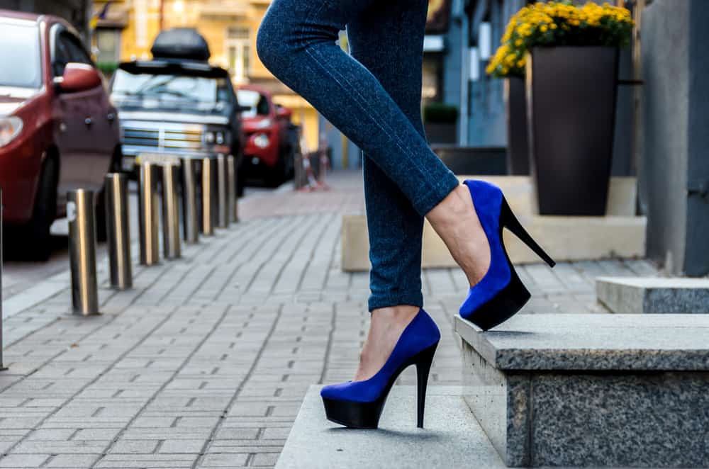 someone in jeans wearing blue and black platform stilettos