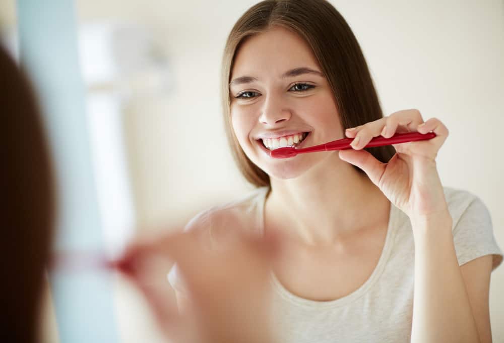 young woman brushing her teeth in front of mirror