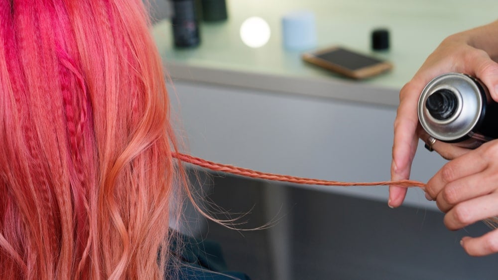 stylist uses hairspray on dyed pink hair