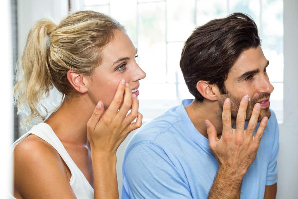 man and woman looking in mirror to apply moisturizer to face