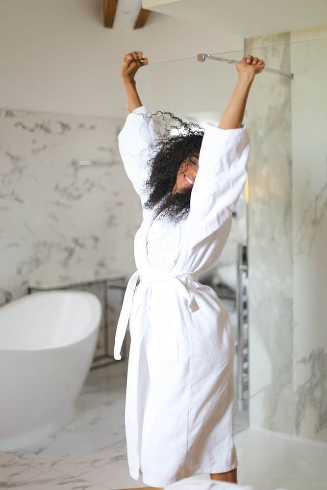 Women in white robe stretches in bathroom