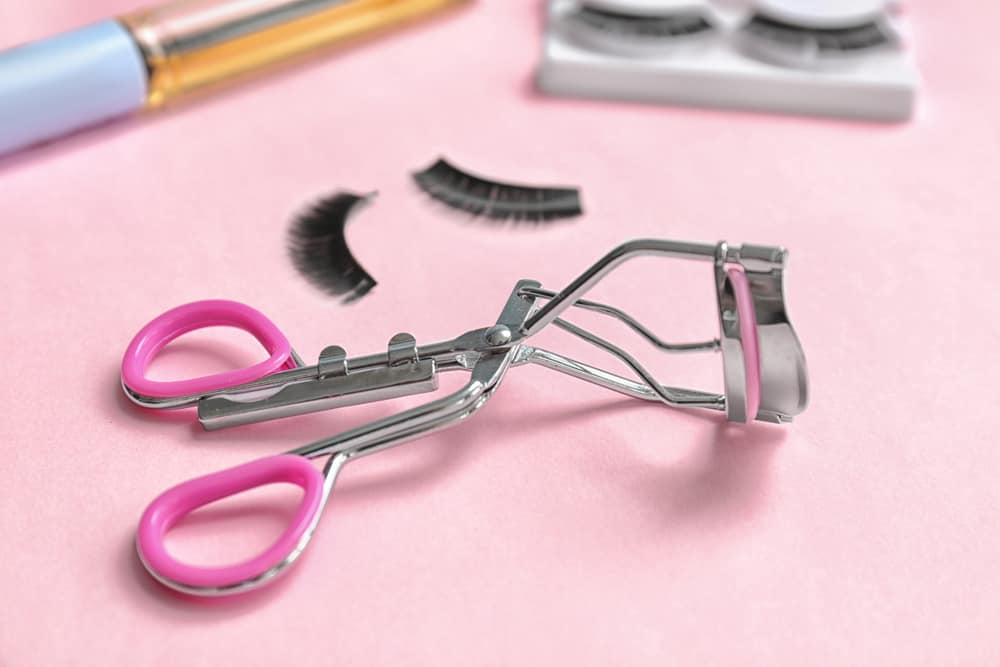 close-up of an eyelash curler and false lashes on a pink background