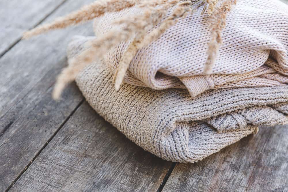 Sweaters on wooden table with dried plant