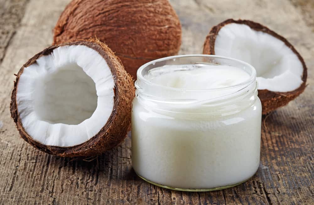 a jar of coconut oil along with fresh coconuts