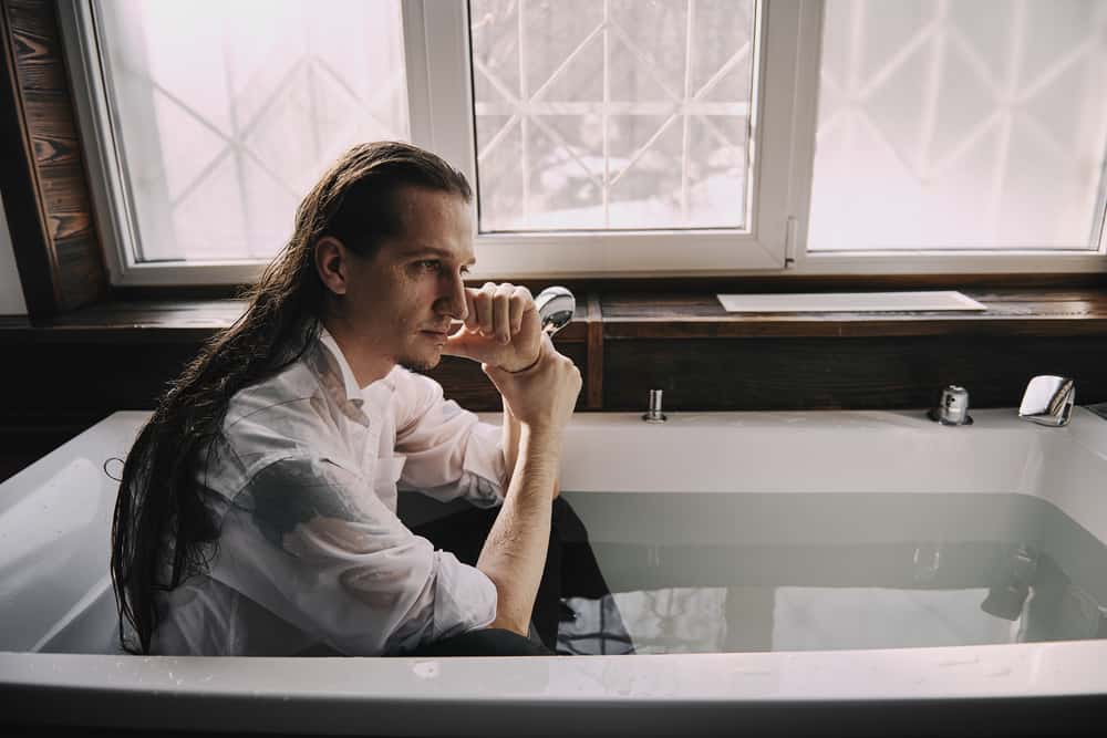 a man sits in a bath of water wearing a pair of jeans