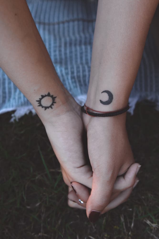 clasped hands with matching Sun and Moon tattoos