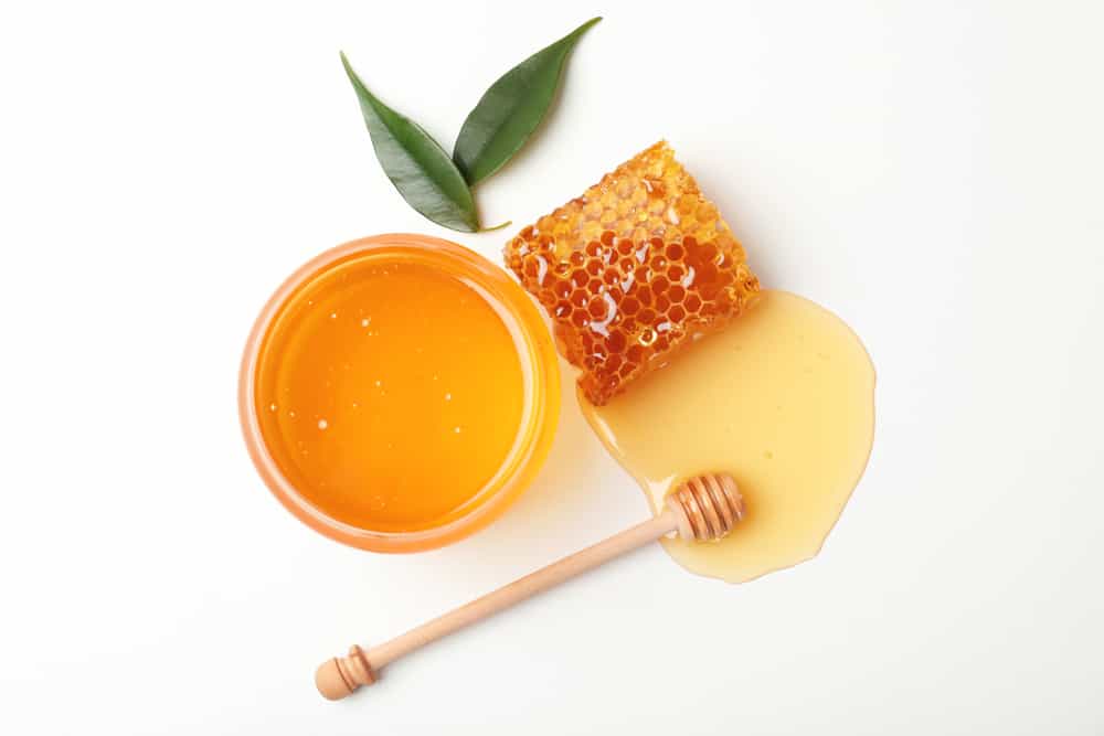 A bowl of honey next to a honeycomb