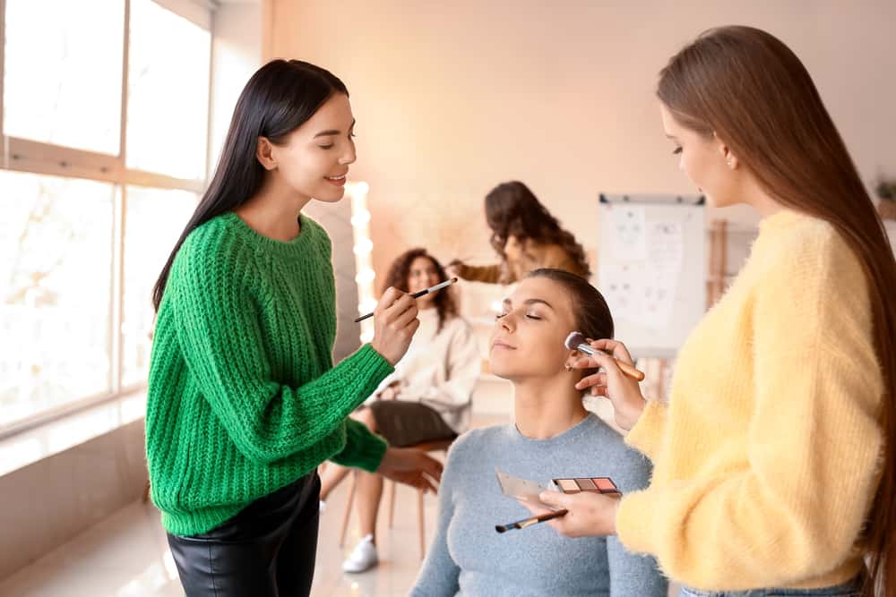 smiling students applying woman’s makeup